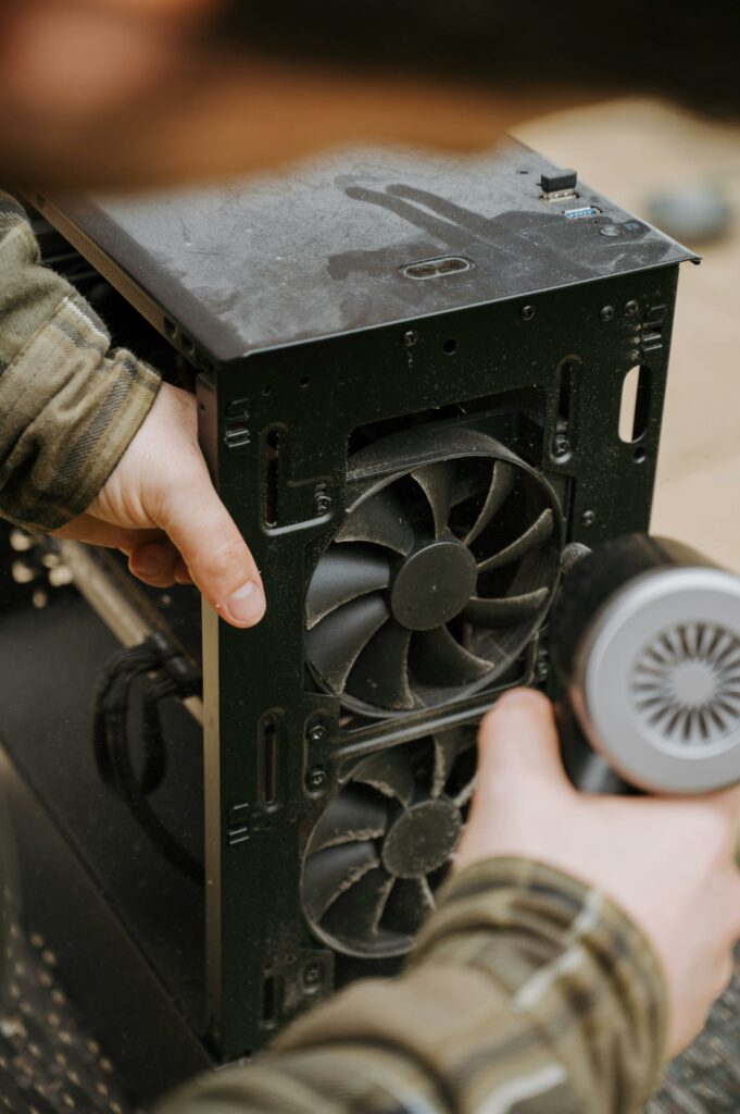 pexels-photo-31854233-31854233 Hands cleaning dust from a computer fan using an electric air duster for maintenance.